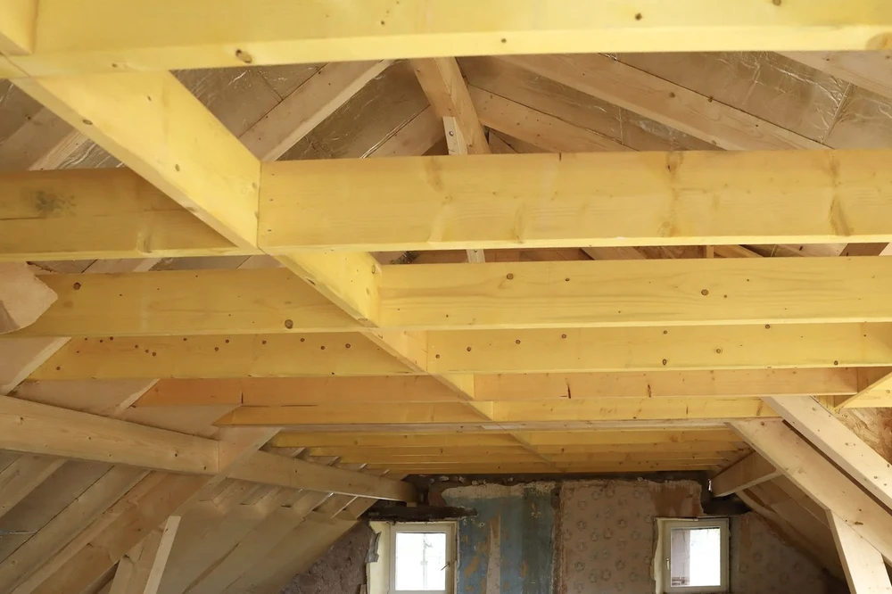 Intérieur d'une construction en cours, charpente en bois apparent avec poutres et solives neuves