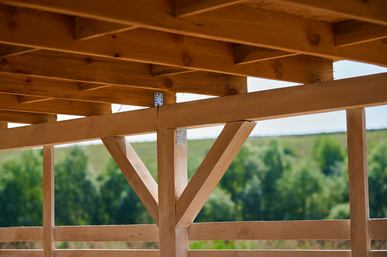 Structure en bois d'une construction en cours, vue depuis l'intérieur vers l'extérieur avec paysage verdoyant en arrière-plan
