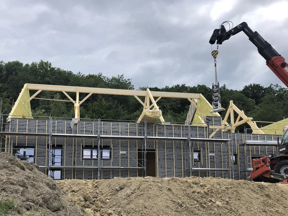 Maison contemporaine en construction avec façade mixte bois et bardage gris, toiture en tuiles métalliques avec système de fixation apparent