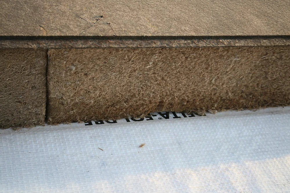 Chantier de construction en cours, ouvrier en combinaison blanche manipulant matériau isolant fibré dans structure bois